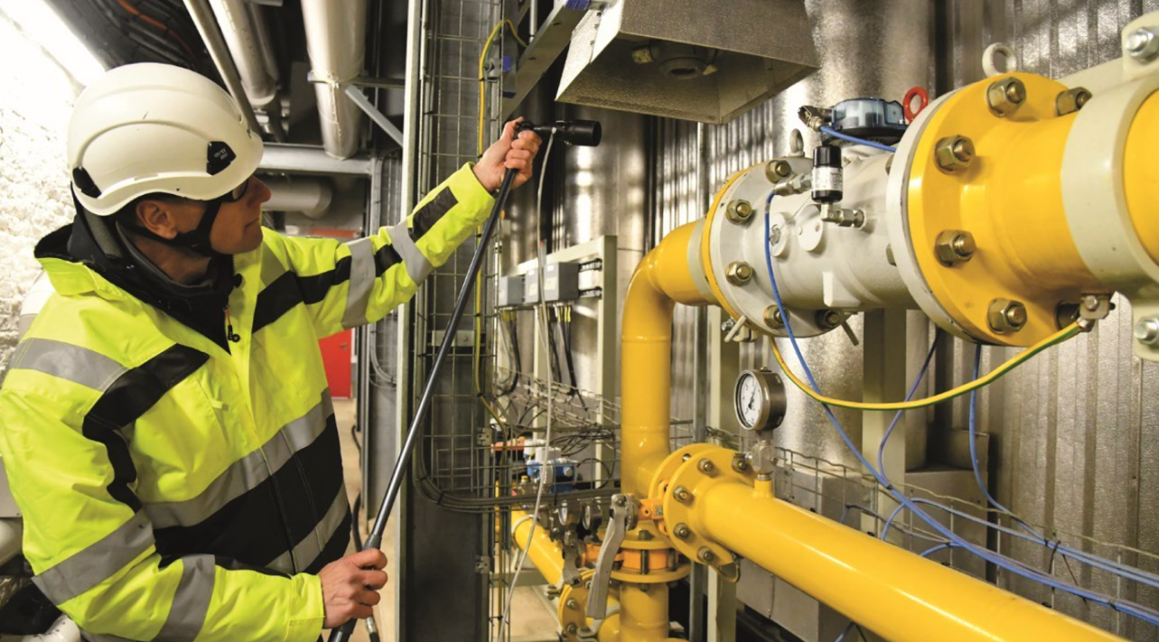 Technicien &eacute;quip&eacute; d'un casque et d'une veste haute visibilit&eacute; inspectant des canalisations et des &eacute;quipements dans une installation industrielle